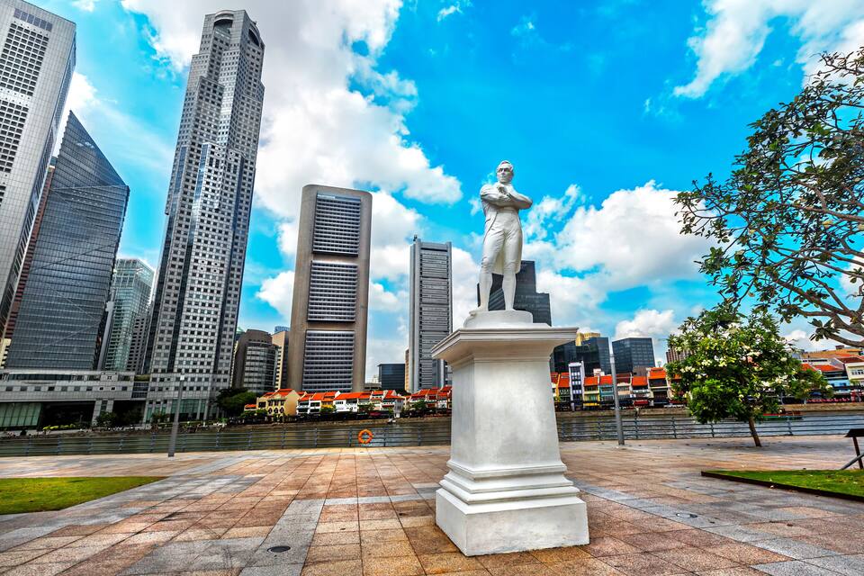 Una estatua en una plaza con edificios modernos y un río al fondo.