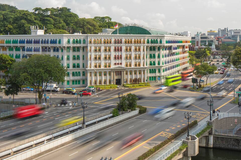 A multi-story building with colorful windows and a green dome, surrounded by a busy intersection and a river.