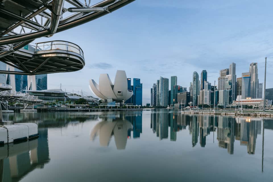 Un paysage urbain au bord de l’eau, caractérisé par une architecture moderne, notamment un bâtiment blanc remarquable aux formes courbes et un pont doté d’une structure métallique.
