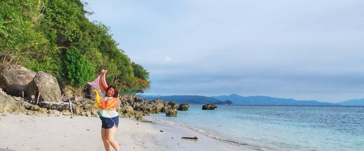 A beach with clear water, rocks, and a hilly landscape in the background.