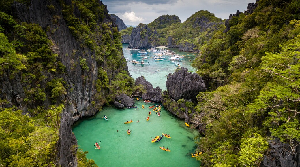 Aerial drone view of a beautiful tropical lagoon filled with kayaks and surrounded by jagged limestone cliffs (Small Lagoon, Miniloc Island, El Nido)