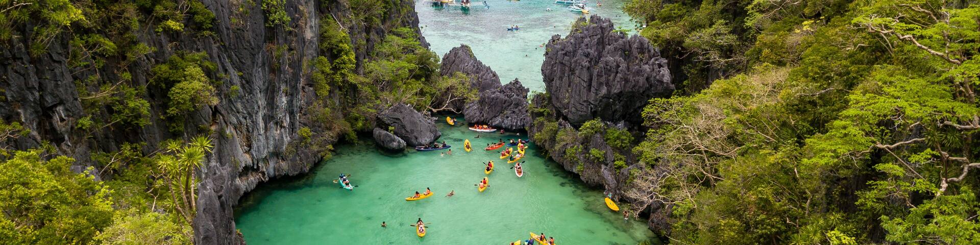 Aerial drone view of a beautiful tropical lagoon filled with kayaks and surrounded by jagged limestone cliffs (Small Lagoon, Miniloc Island, El Nido)