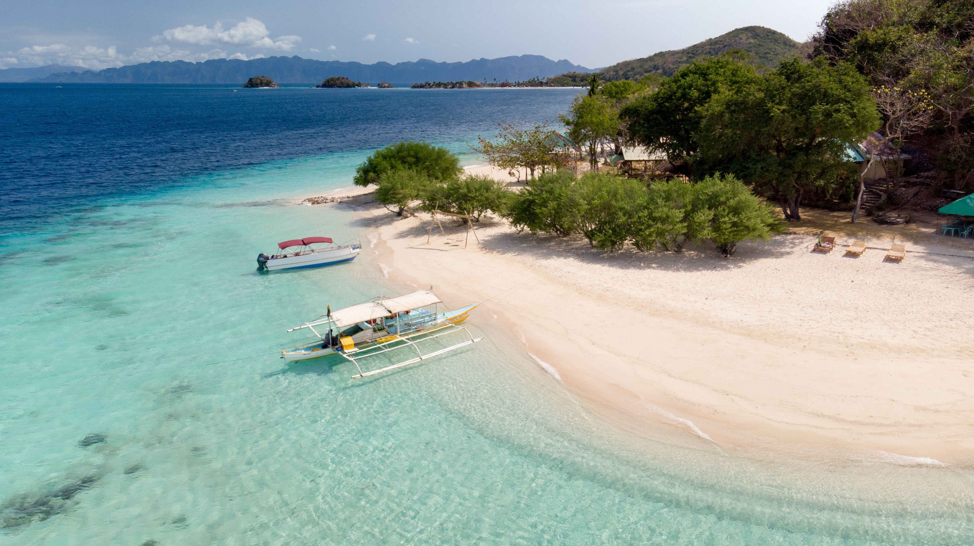 Aerial view of Banana Island, a white sand tropical beach with turquoise waters, palm trees, and a traditional bangka boat in Coron, Palawan, Philippines