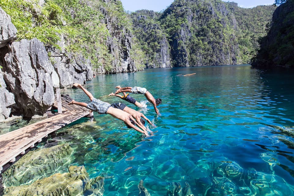 A clear blue water body with rocky cliffs and lush greenery.