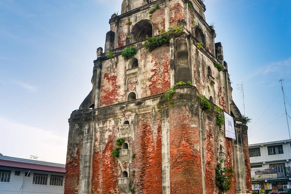 An old, weathered church with a bell tower, surrounded by modern buildings.