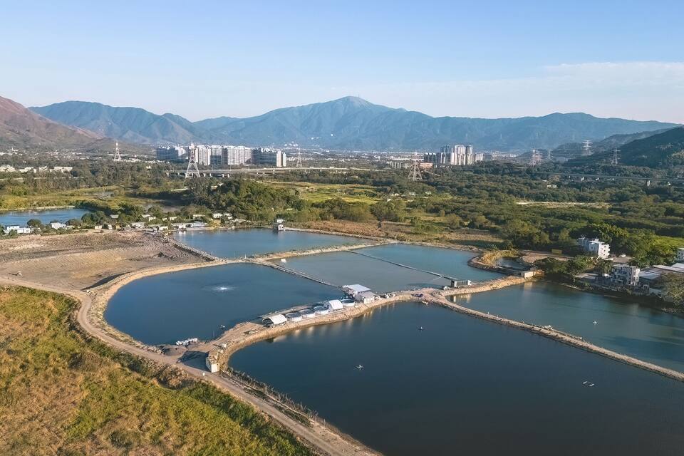 Un río con varios estanques, un puente y un paisaje urbano con montañas al fondo.