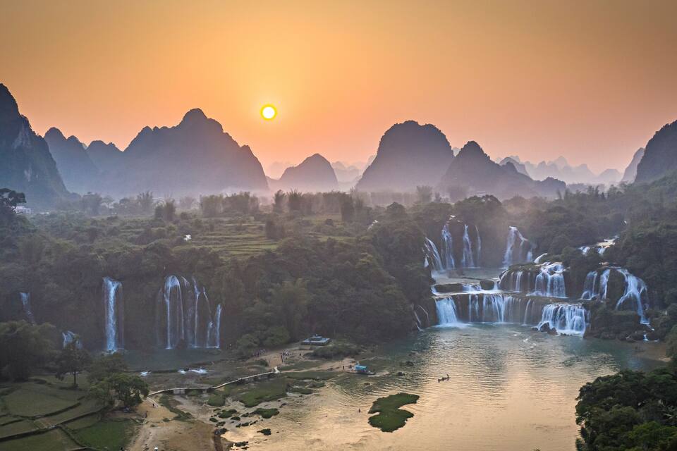 Un río con numerosas cascadas, rodeado de abundante vegetación y montañas.