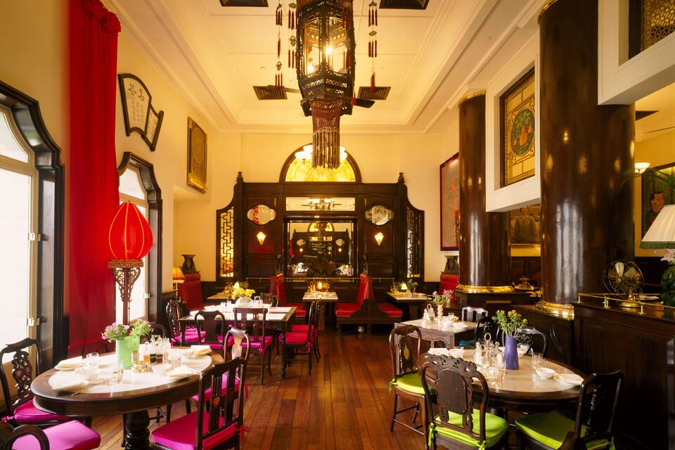 A traditional restaurant interior with wooden floors, red and green upholstered chairs, and ornate decorations.