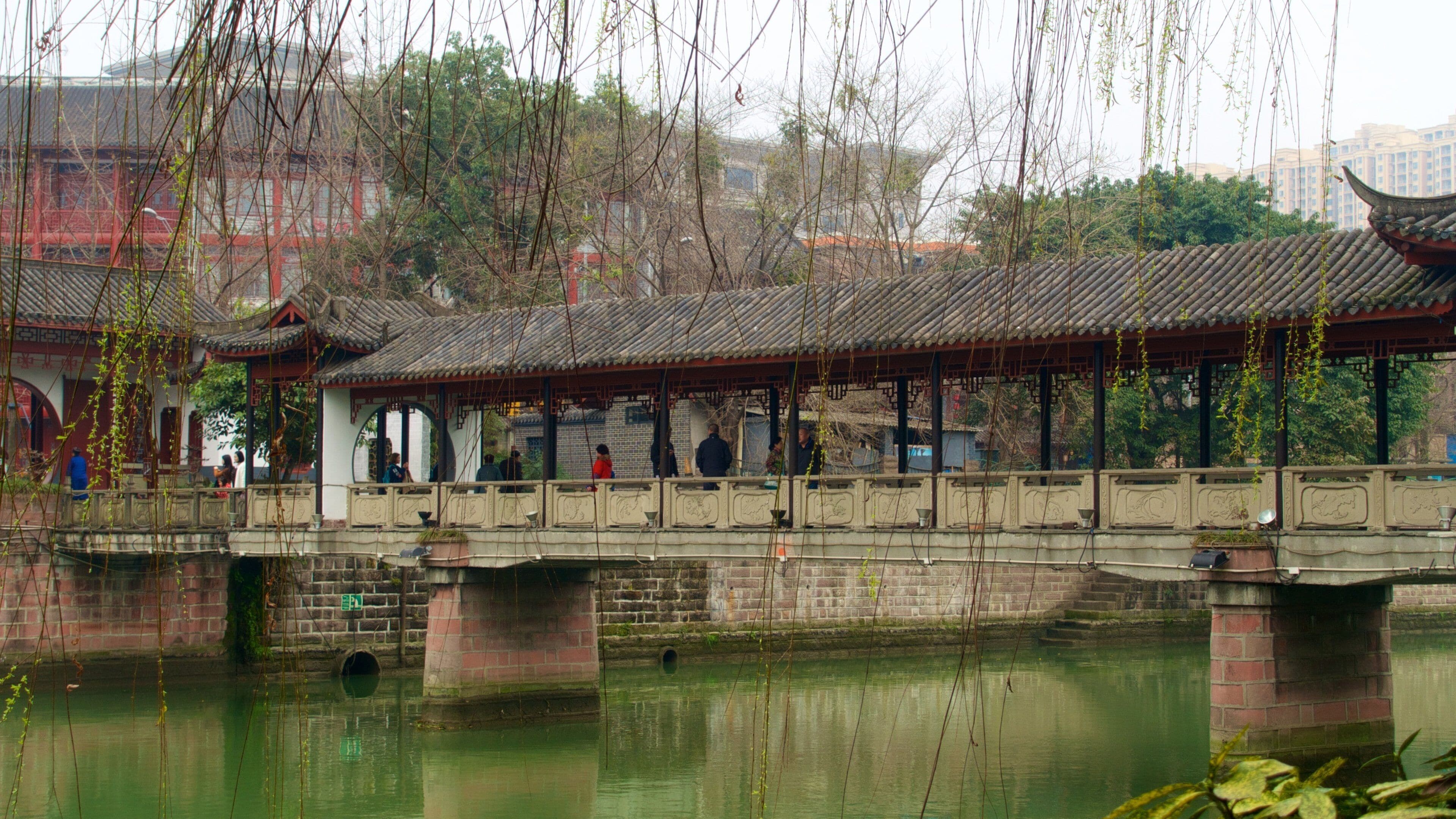 A traditional Chinese pavilion over a canal with people walking on the bridge.