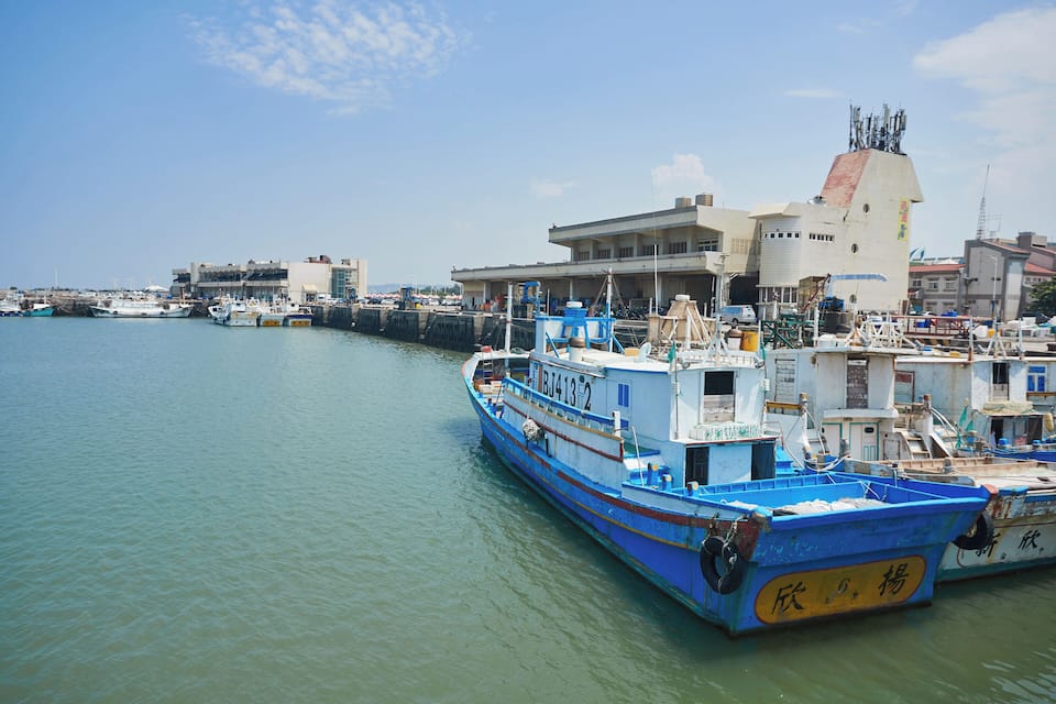 A harbor with boats docked, a large building, and a clear sky.
