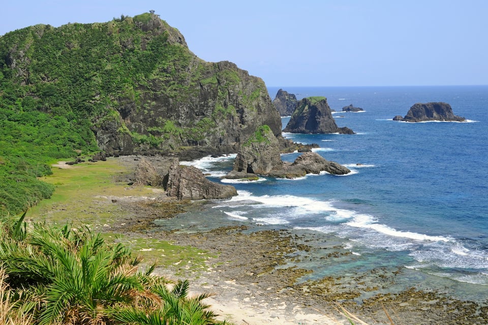 A coastal landscape with rocky cliffs, green vegetation, and clear blue waters.