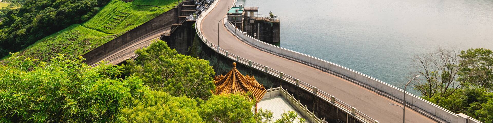 Un puente curvo sobre un lago tranquilo, rodeado de verdes colinas y un cielo azul despejado.