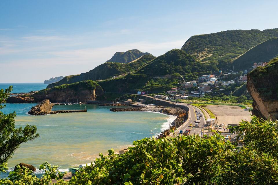 Un pueblo costero con playa, acantilados y una carretera que lleva al mar.