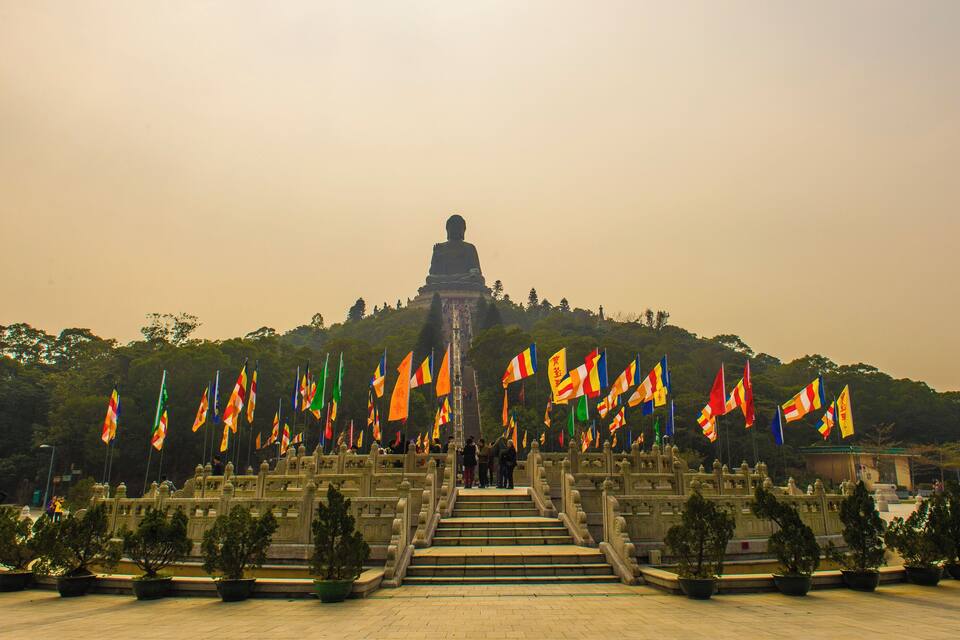 A large Buddha statue on a hill with many flags in front.