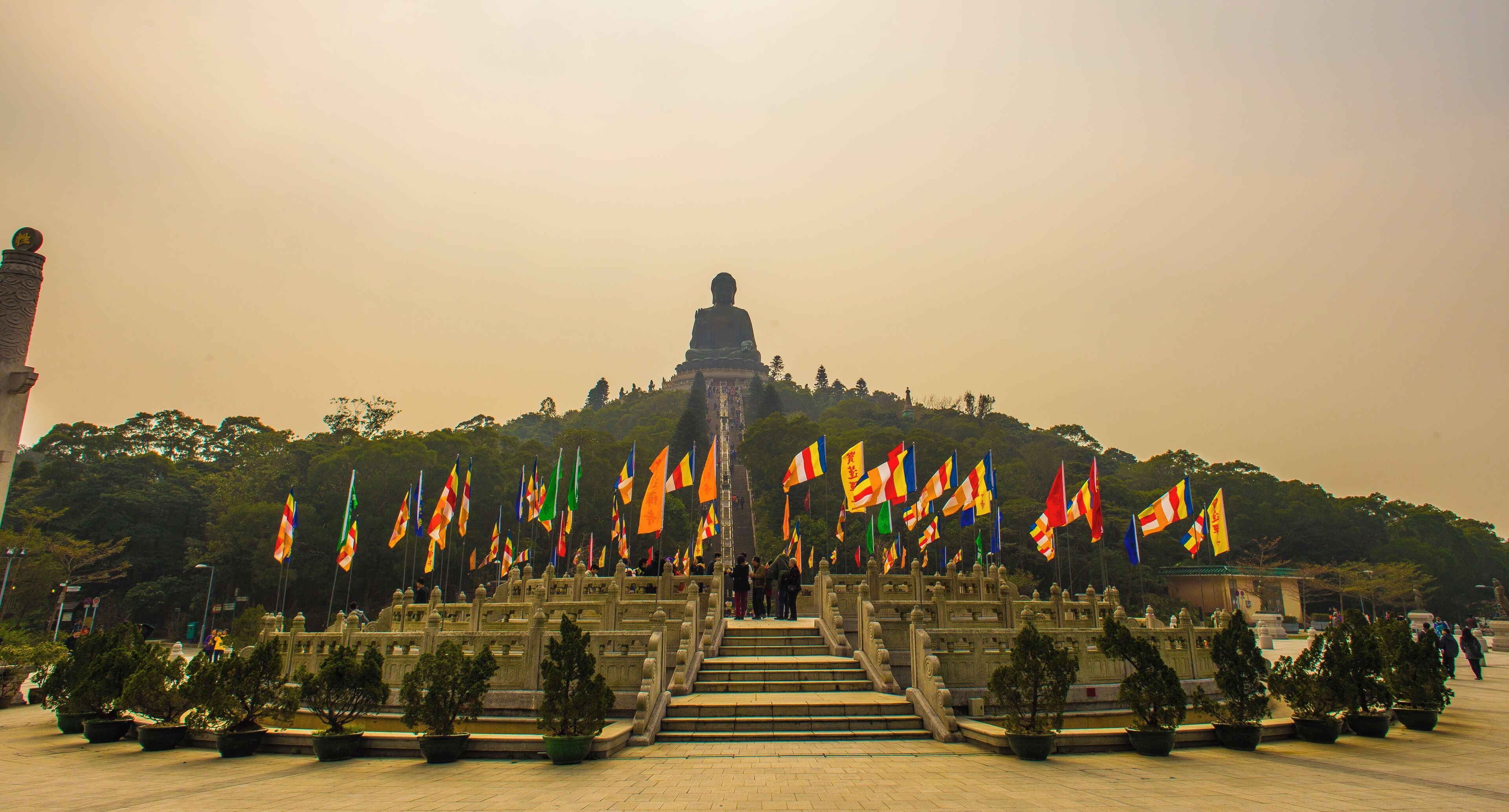 A large Buddha statue on a hill with many flags in front.