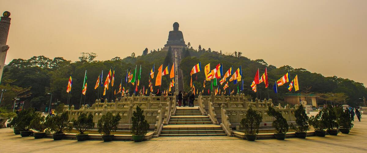 A large Buddha statue on a hill with many flags in front.
