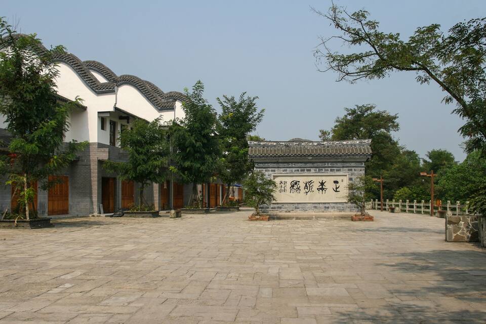 A courtyard with traditional architecture, including a building with a tiled roof and a stone wall with inscriptions.