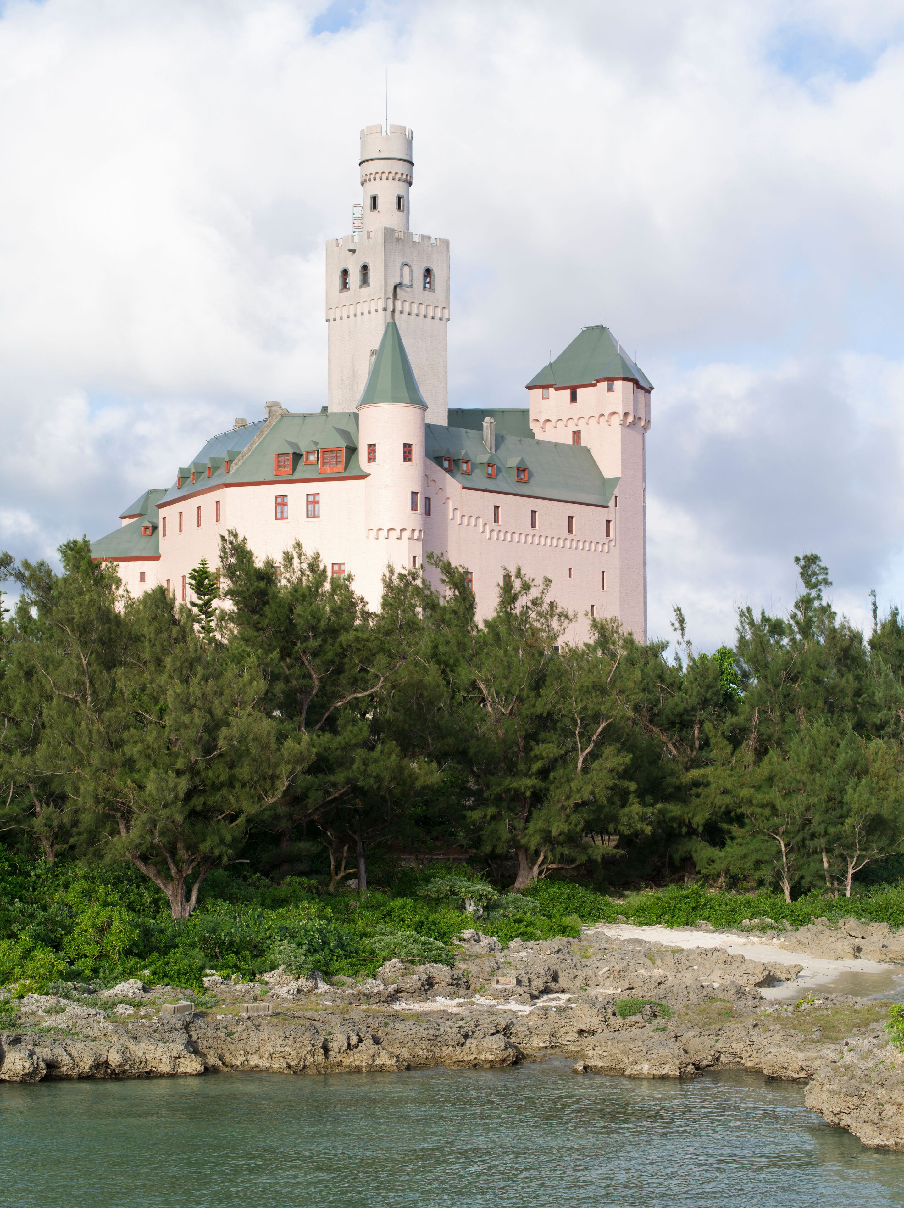 A castle with a tower, surrounded by trees and a body of water.