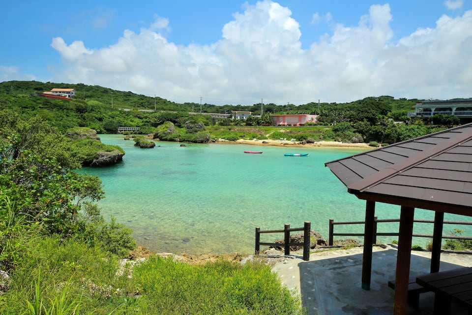 A coastal landscape with clear turquoise waters, rocky outcrops, and a wooden pier.