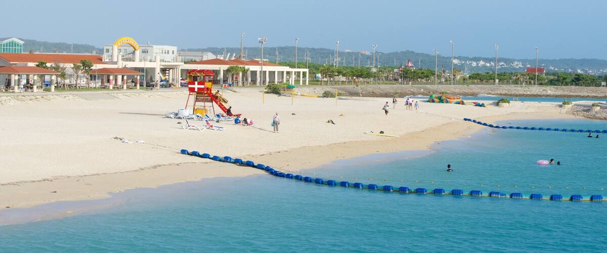 A beach with lifeguard towers, a swimming area, and a building with a red roof.