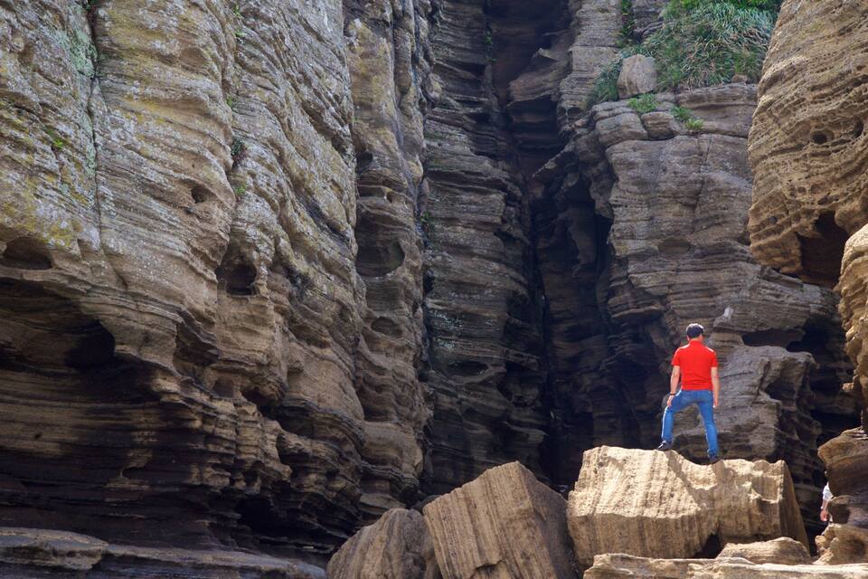 A person standing on a rock ledge in a canyon with layered rock formations.
