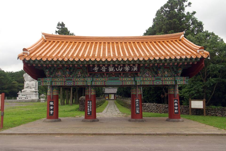 A traditional Chinese gate with intricate designs and a tiled roof, leading to a statue and a pathway.