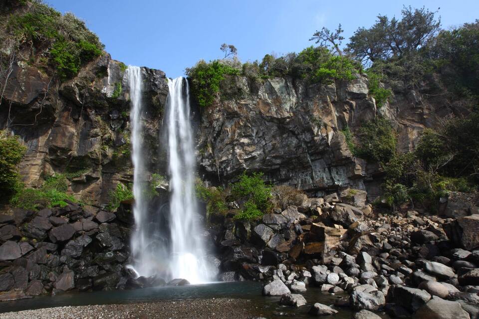 Uma cascata desce por um penhasco rochoso, cercada por vegetação.