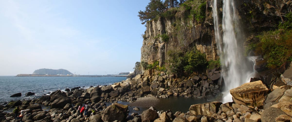 Jeongbang Waterfall featuring rocky coastline, a cascade and general coastal views