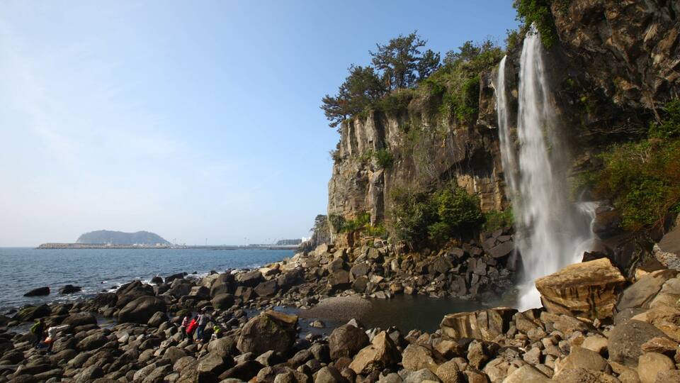 Jeongbang Waterfall featuring rocky coastline, a cascade and general coastal views