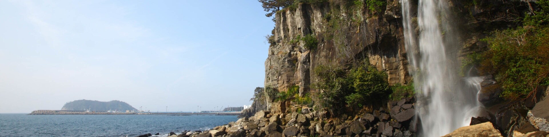 Jeongbang Waterfall featuring rocky coastline, a cascade and general coastal views