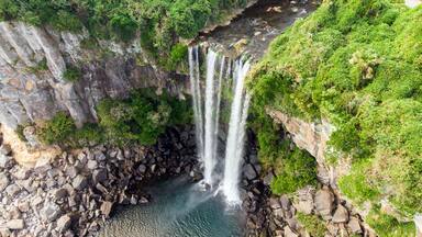 Una cascada de varios niveles que se precipita en un estanque rocoso rodeado de abundante vegetación.