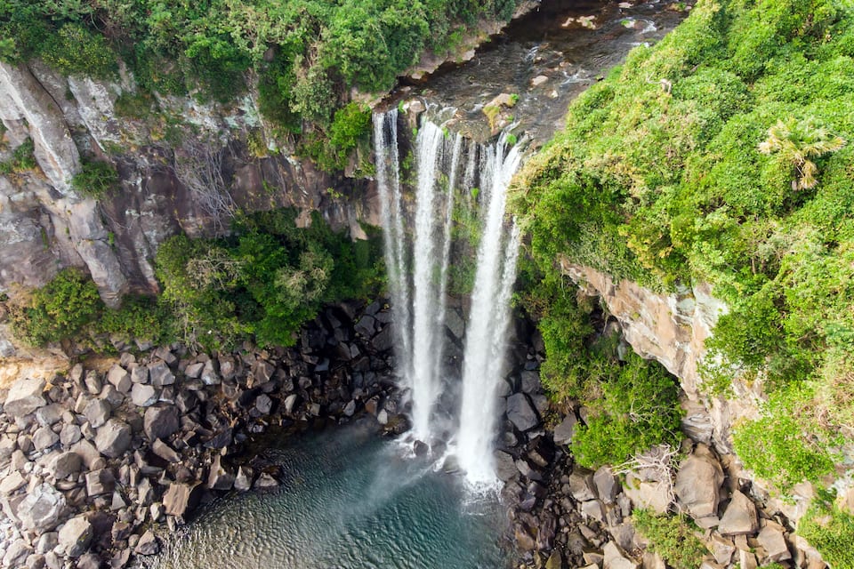Una cascada de varios niveles que se precipita en un estanque rocoso rodeado de abundante vegetación.