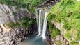 Una cascada de varios niveles que se precipita en un estanque rocoso rodeado de abundante vegetación.