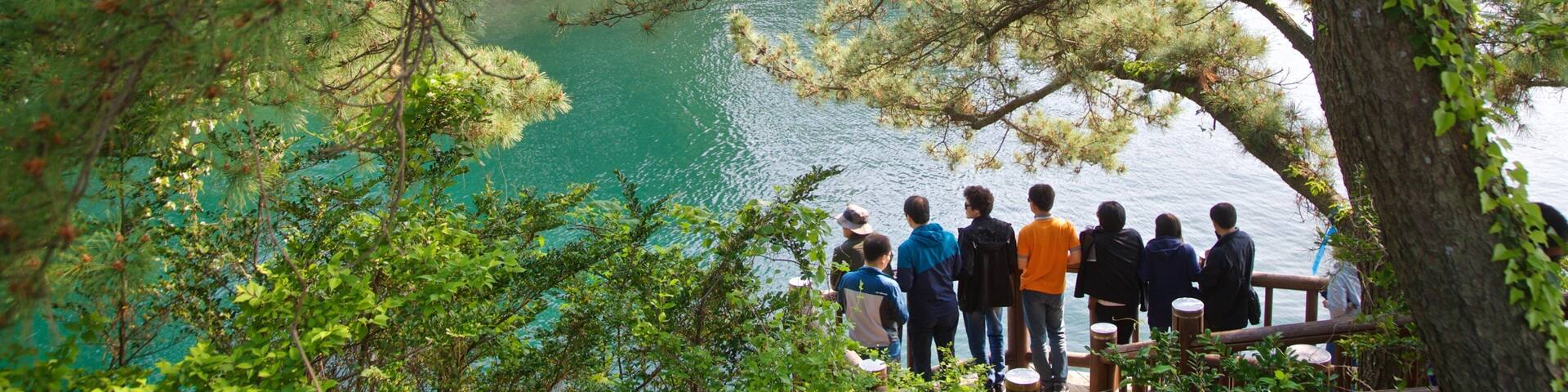 A group of people standing on a wooden deck overlooking a turquoise lake surrounded by trees.