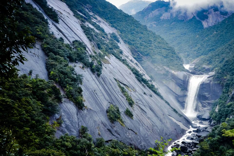 Ein Wasserfall stürzt über einen steilen, felsigen Berg, umgeben von dichtem Grün.