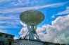 A large satellite dish against a blue sky with clouds.