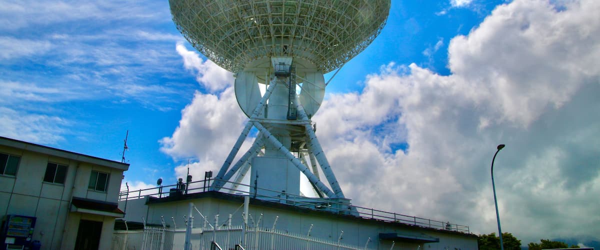 A large satellite dish against a blue sky with clouds.