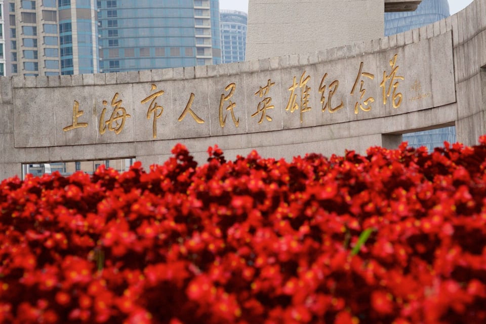 A building with a large sign in Chinese characters and a field of red flowers in the foreground.