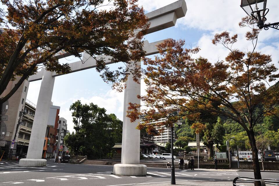 A large stone torii gate in a park with autumn trees and modern buildings in the background.