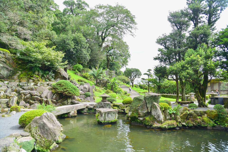 Um jardim tranquilo com lago, pedras e vegetação exuberante.