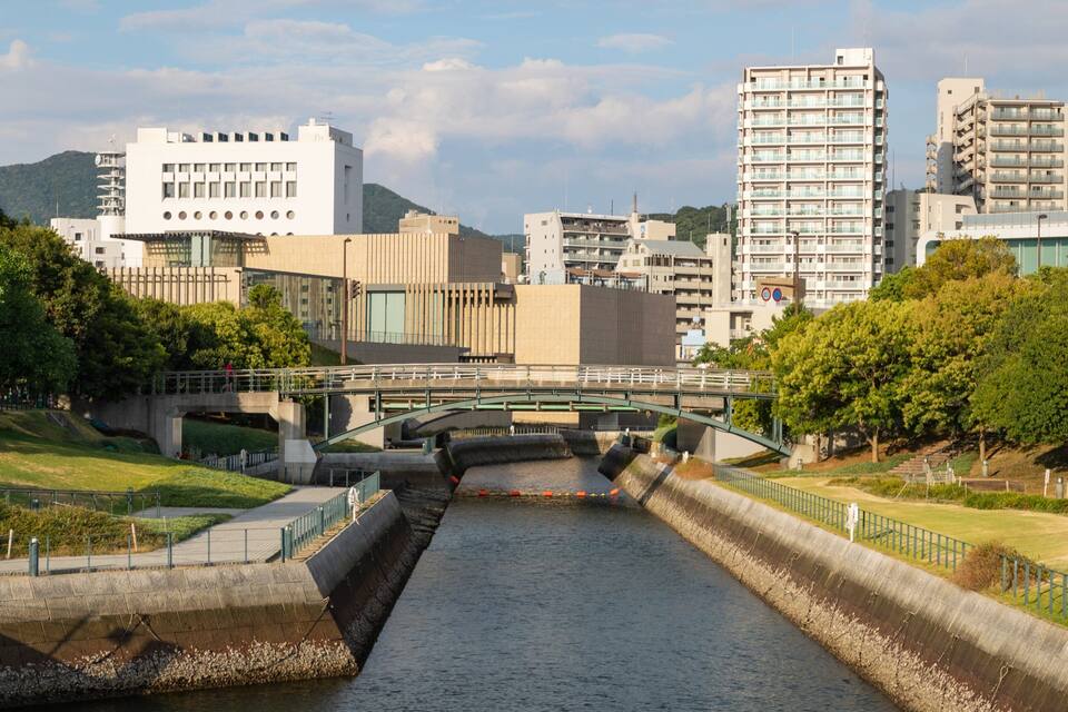 A river with a bridge, surrounded by greenery and modern buildings.