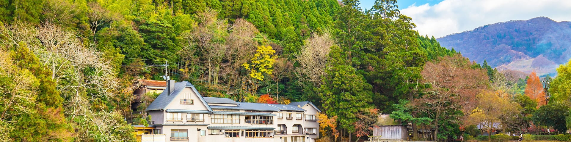 A serene lake with a traditional Japanese house reflecting on the water, surrounded by lush greenery and mountains.