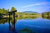 A serene lake with a traditional Japanese torii gate in the foreground, surrounded by lush greenery and mountains in the background.