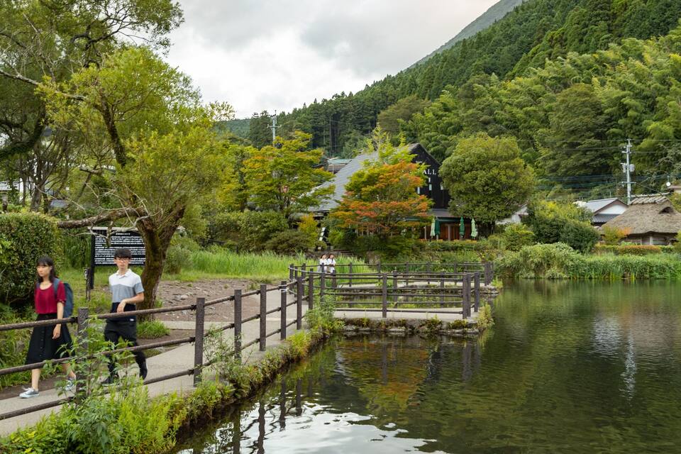 A wooden bridge over a calm river, surrounded by lush greenery and traditional buildings.