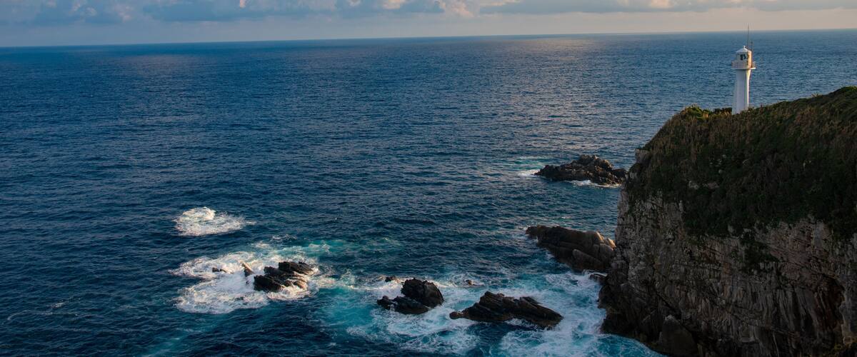 A lighthouse on a cliff overlooking the ocean with waves crashing against the rocks.