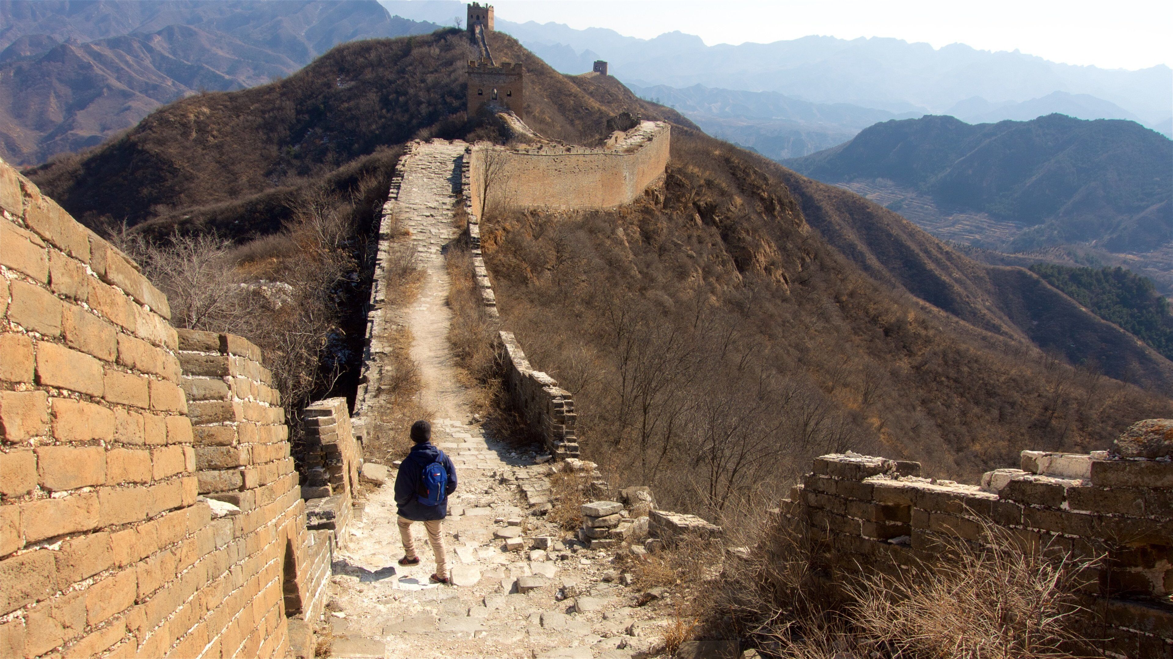 A person walking along the Great Wall of China, with mountainous terrain in the background.