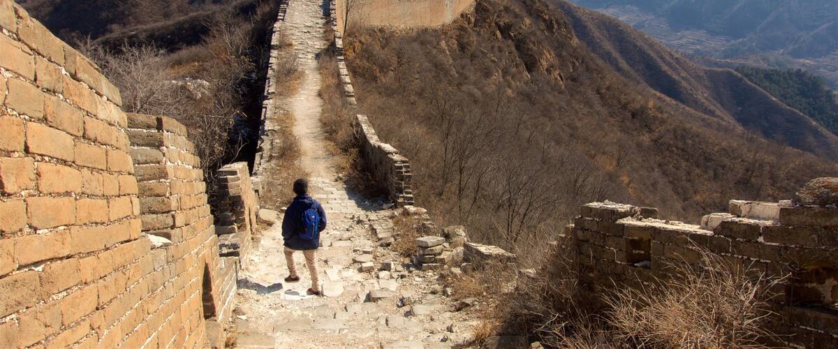 A person walking along the Great Wall of China, with mountainous terrain in the background.