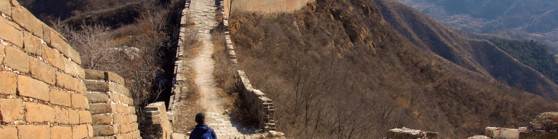 A person walking along the Great Wall of China, with mountainous terrain in the background.