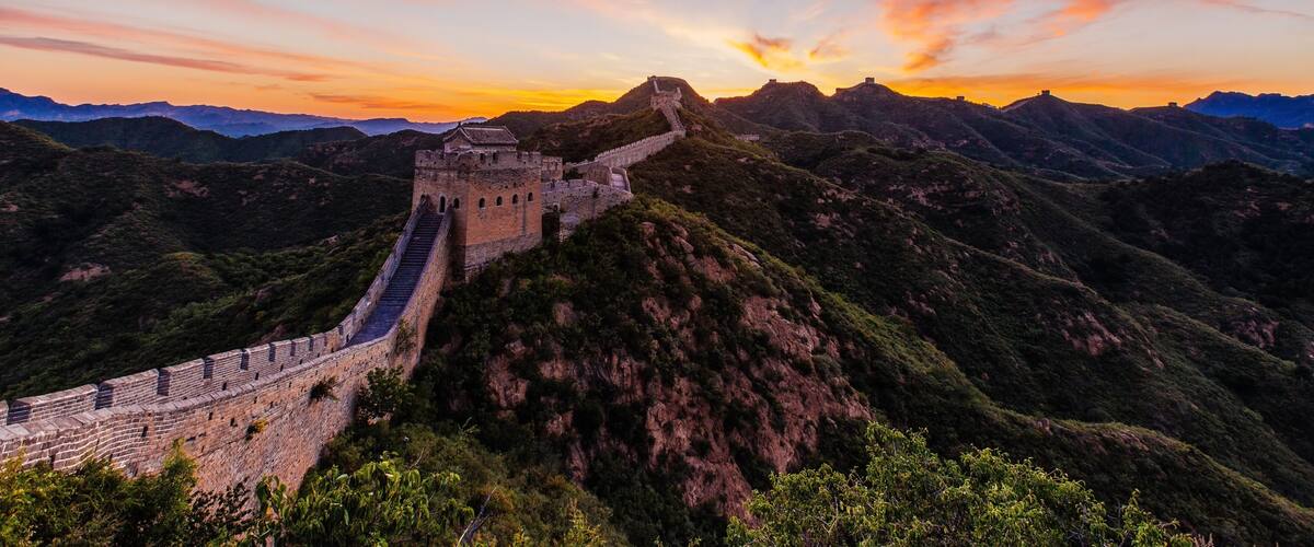 The Great Wall of China winding through mountainous terrain during sunset.