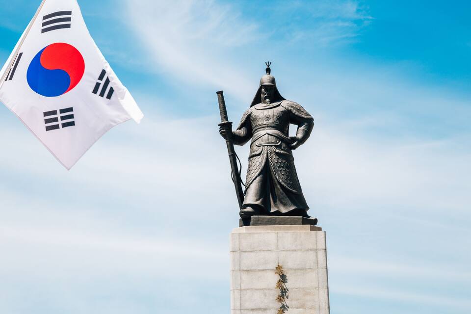 A statue of a warrior holding a sword, with a South Korean flag in the background.